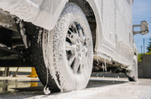 RV Camper Van Covered by Active Washing Foam Close Up Photo. Washing Recreational Vehicle Motorhome in a Car Wash.